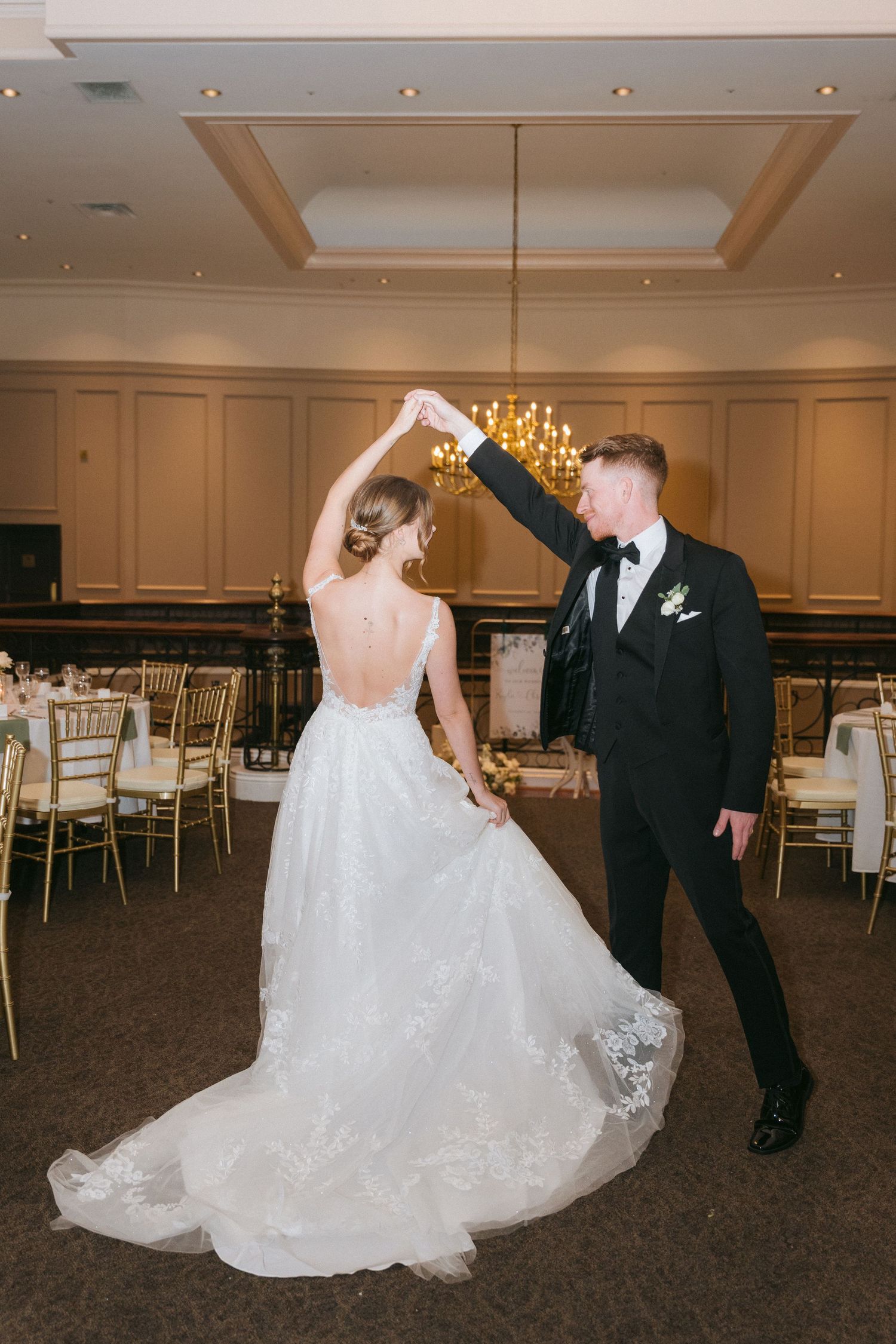 A couple performs a romantic dance sequence in a ballroom with elegant decor and gold chairs.