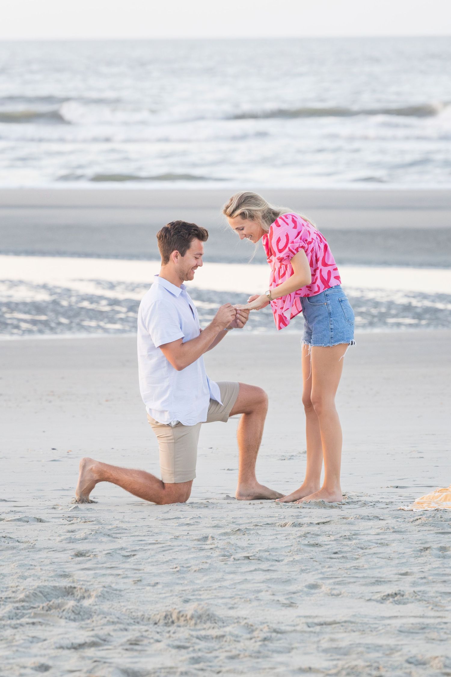A romantic beach proposal scene unfolds with a couple on the sandy shore as waves roll in the background.