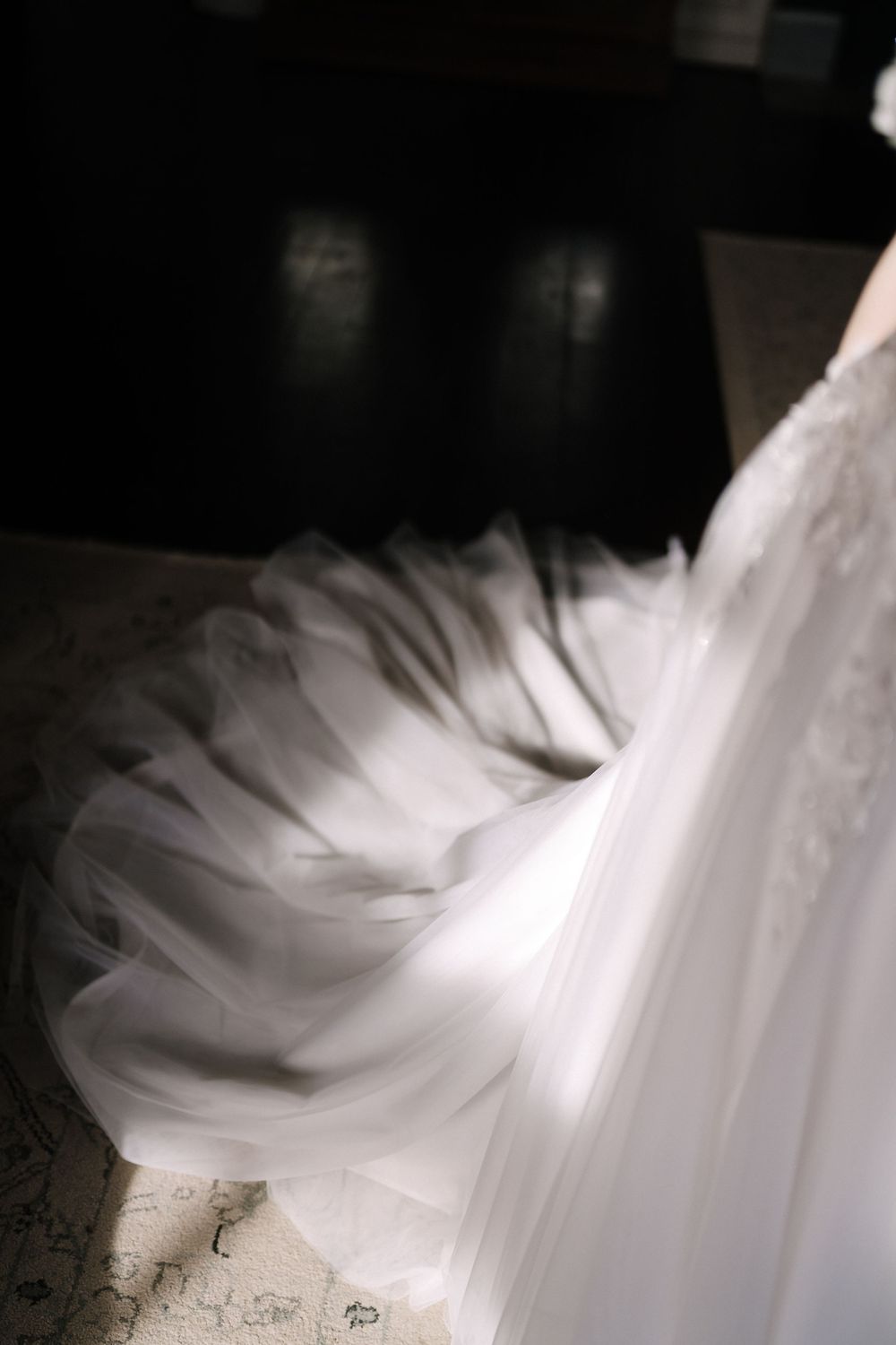 Close-up detail of white tulle fabric from a wedding dress creating elegant flowing layers in dramatic lighting.