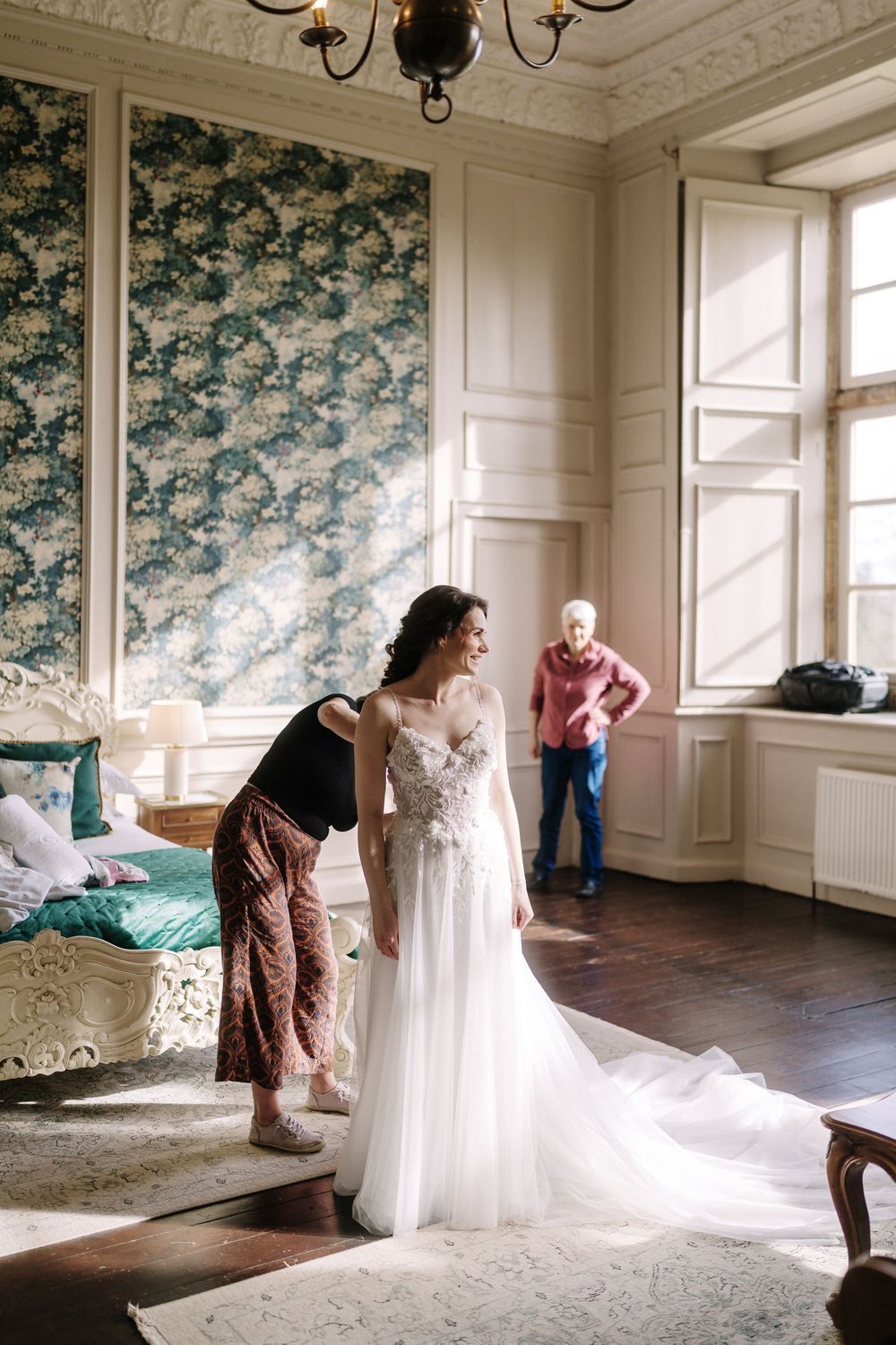 A sequence showing preparations with a white wedding dress in an elegant room with floral wallpaper.
