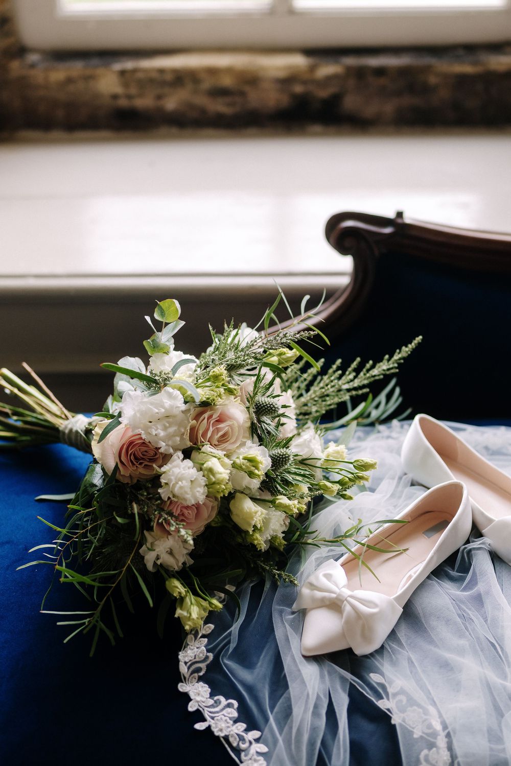 Wedding details featuring elegant white floral arrangements with greenery alongside delicate tulle fabric and ivory bridal shoes.