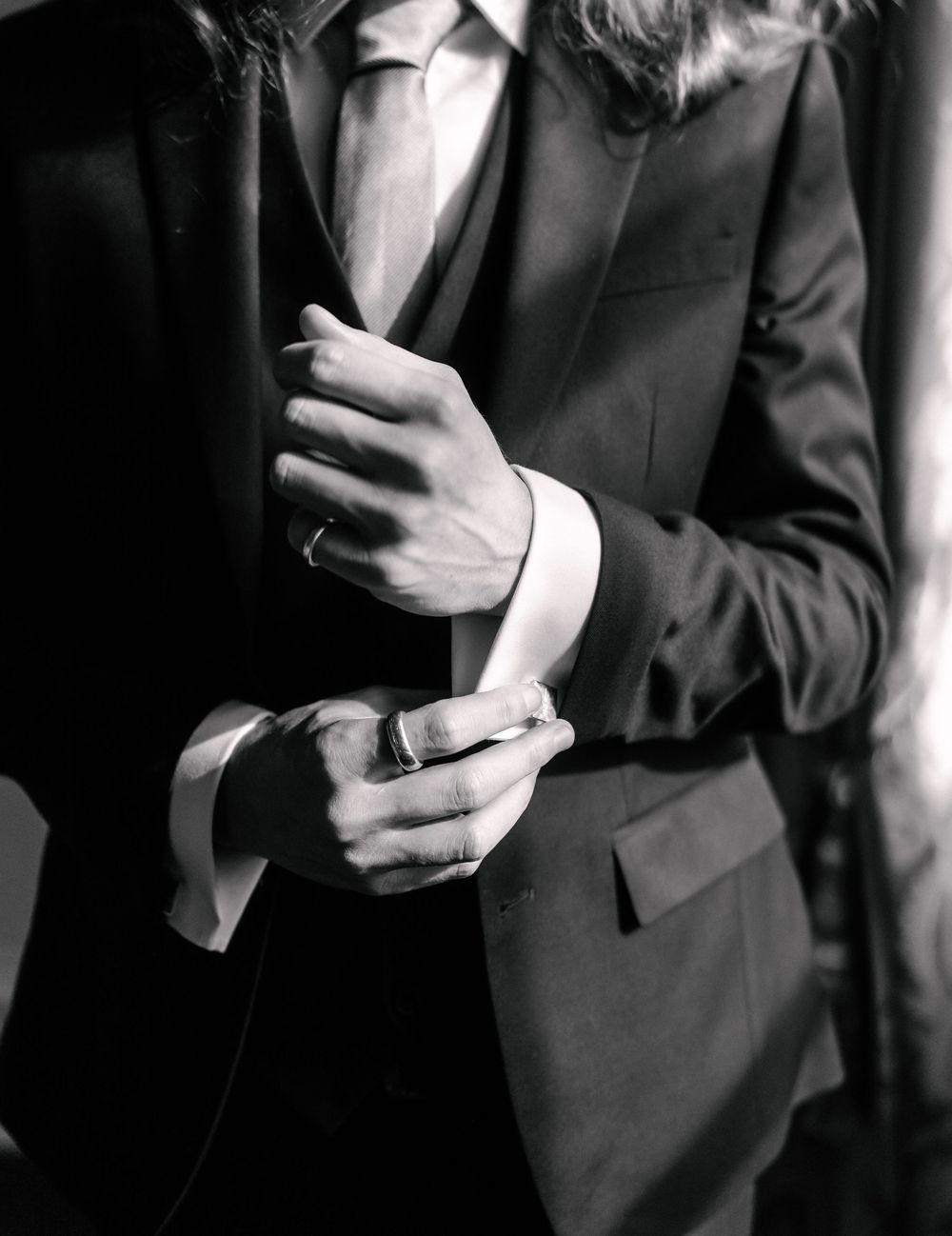 Black and white close-up of hands adjusting suit cuff and sleeve in formal attire.