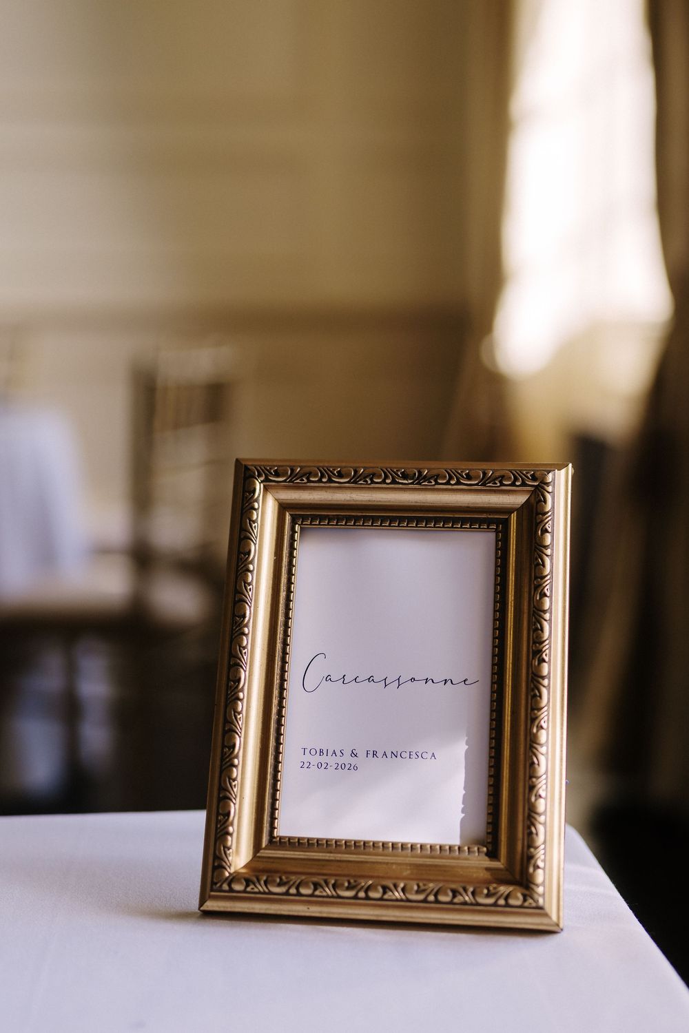 Gold ornate picture frames with place cards displayed on a white surface in soft focus lighting.