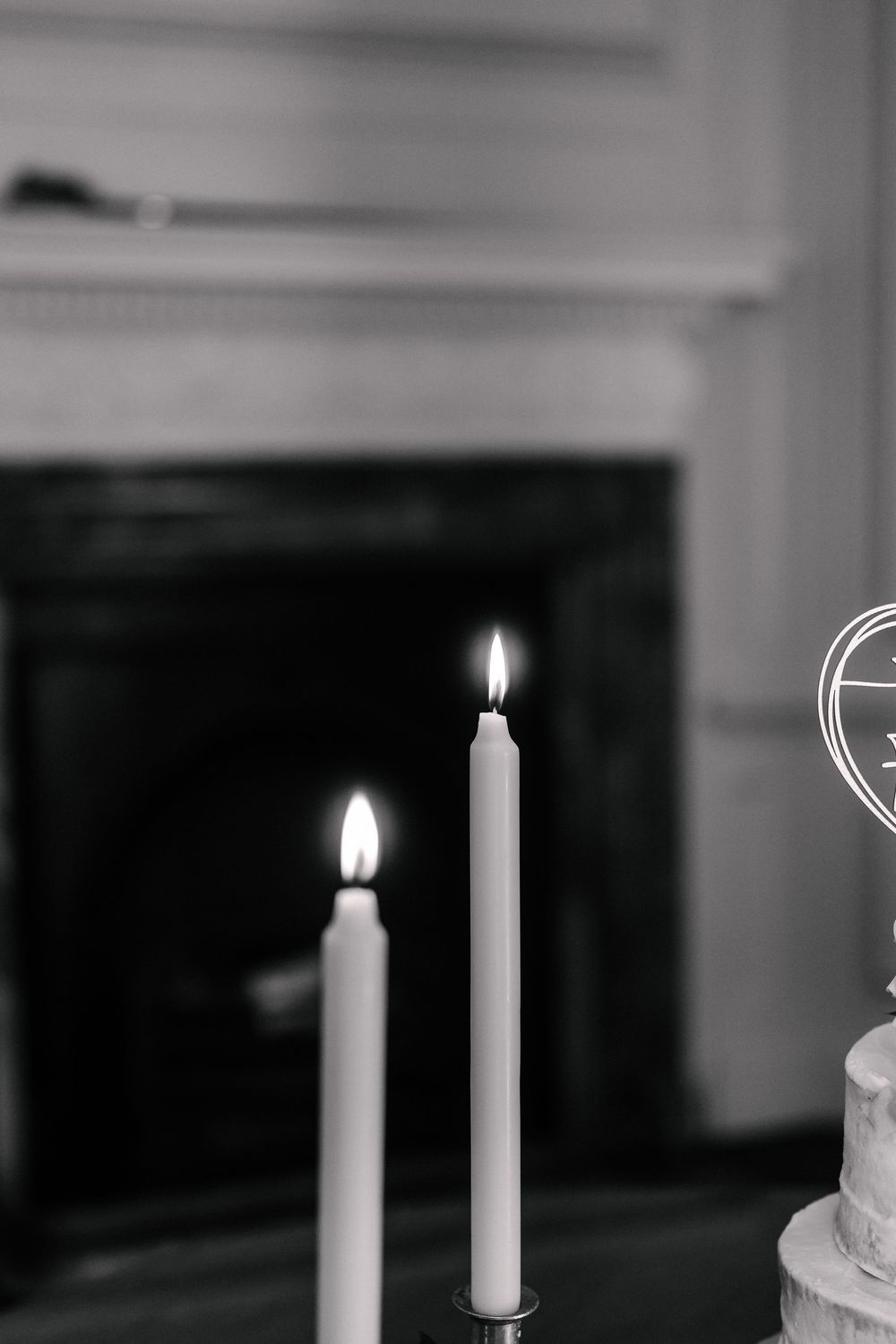 A black and white photograph shows a burning white candle with a glowing flame against a dark background.