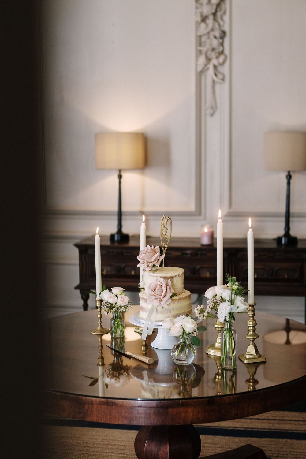 Elegant wedding table centerpiece with white candles, flowers, and delicate glass vases on a dark wooden surface.