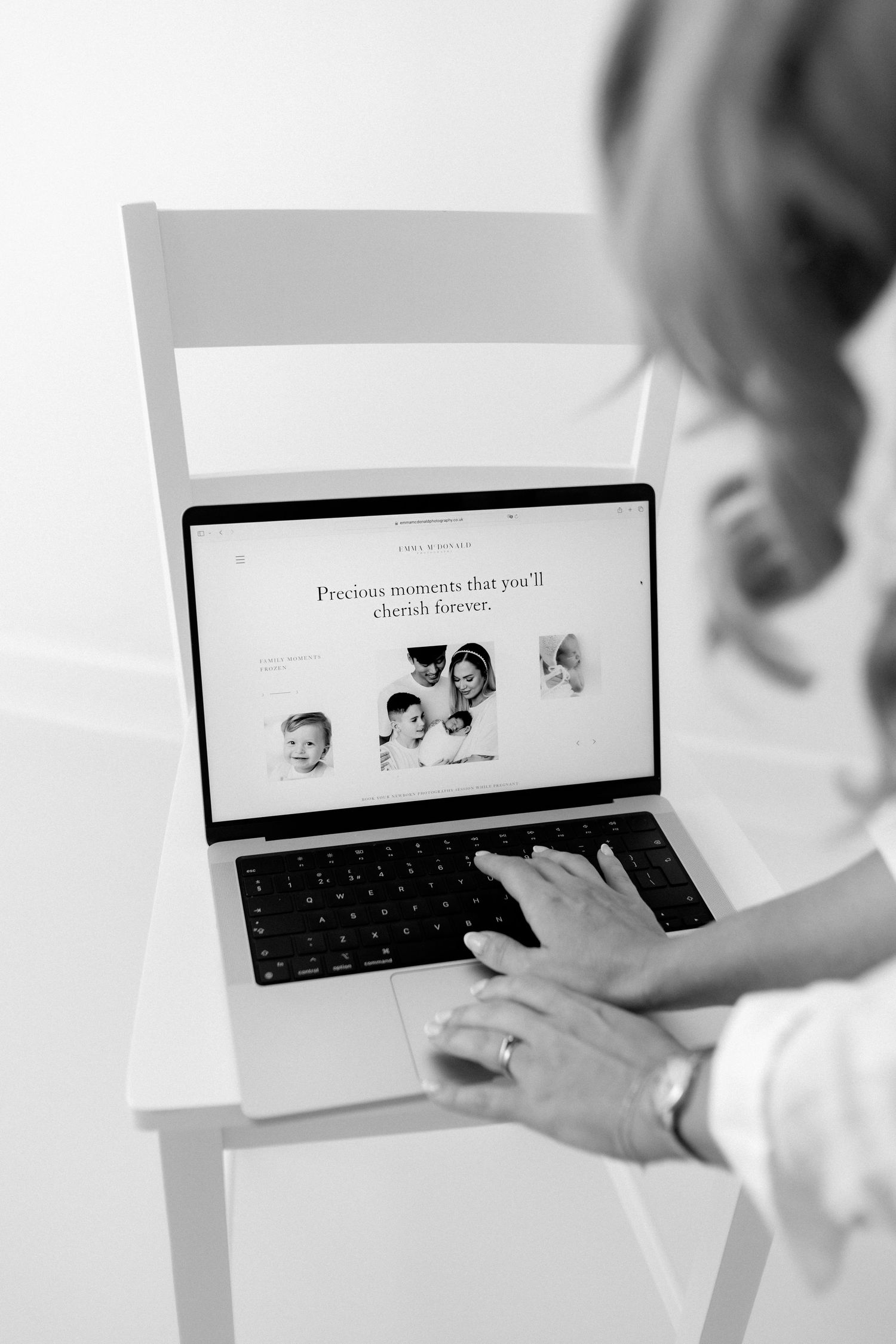 Person working on laptop displaying black and white photographs on screen in monochromatic setting.