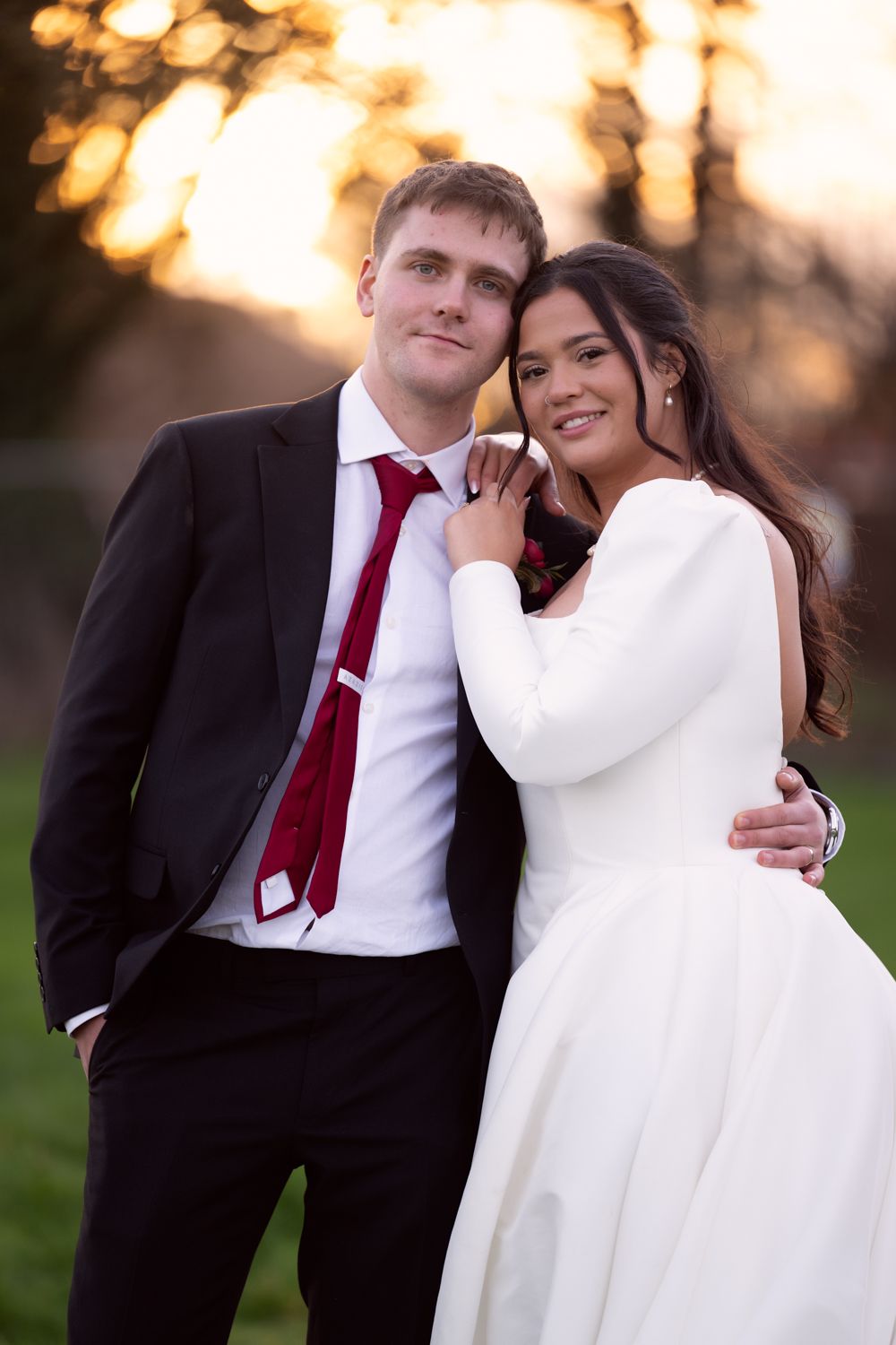 A couple in wedding attire embraces during golden hour sunset in a romantic outdoor photo series.