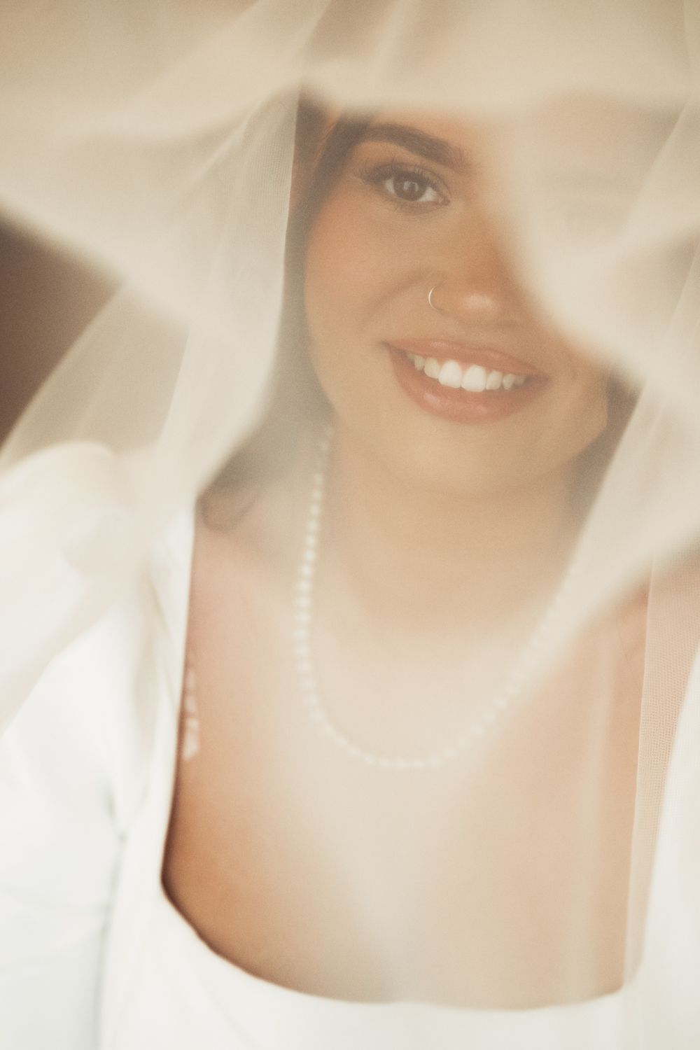 Soft ethereal portrait through sheer white fabric showing a bright smile and warm lighting.