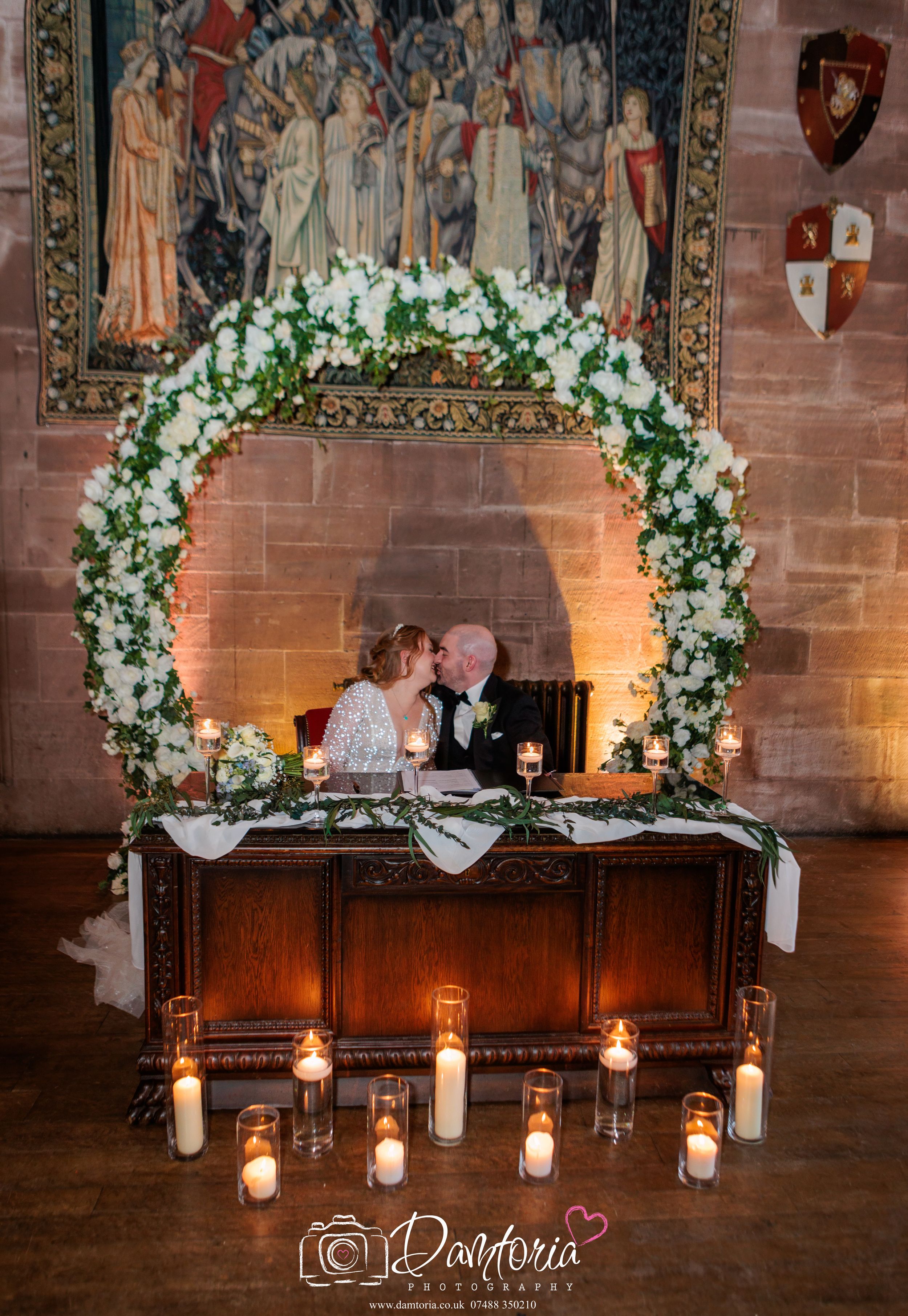 A romantic wedding ceremony setup with floral arches and hanging lanterns in a historic stone church interior.