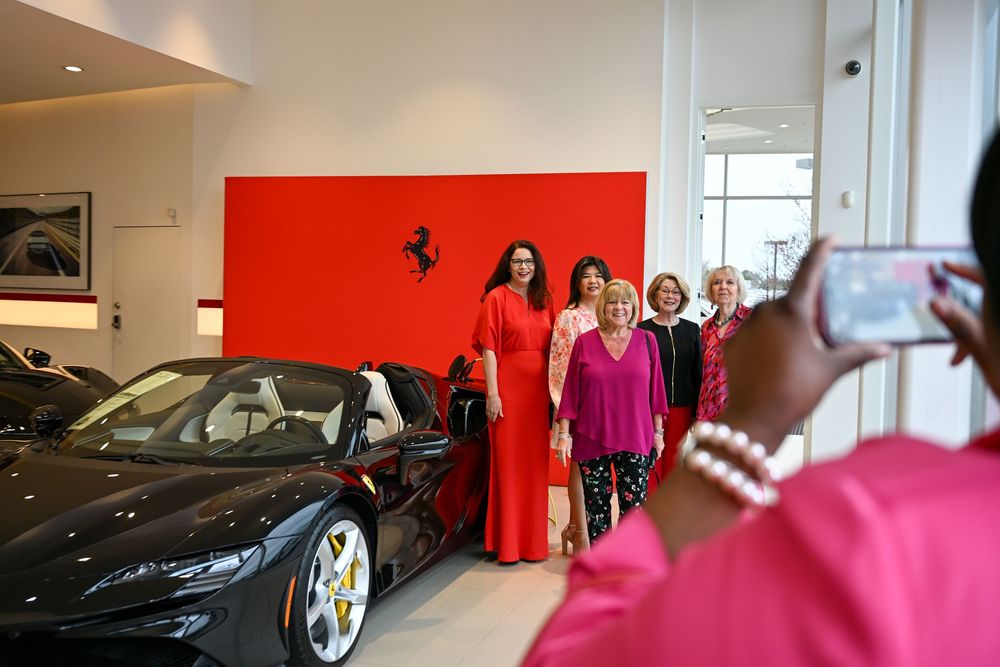 A luxurious Ferrari dealership showroom interior with red walls and multiple sports cars on display.