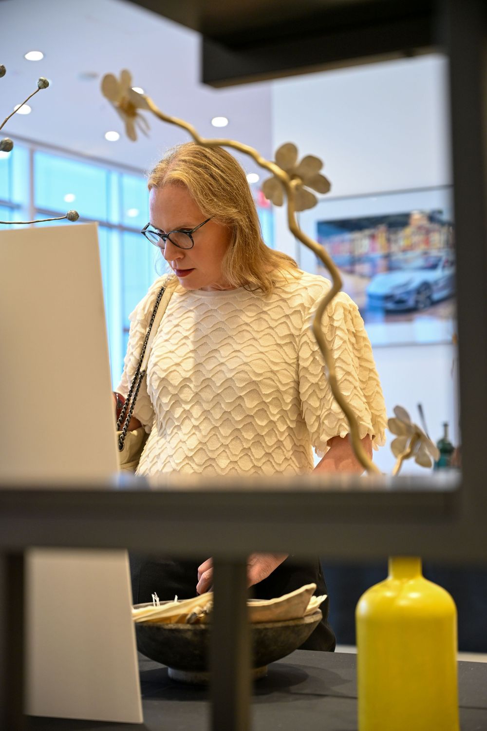 A person in a cream sweater sits at a desk with a yellow bottle visible in the foreground.