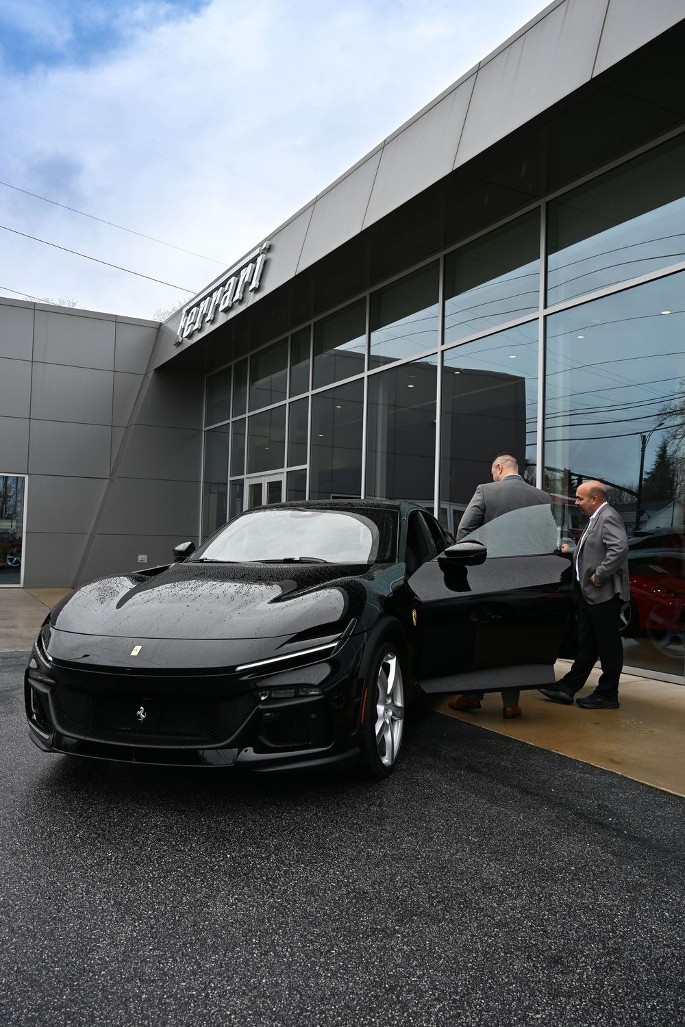 A sleek black McLaren sports car is displayed in front of a modern car dealership showroom.