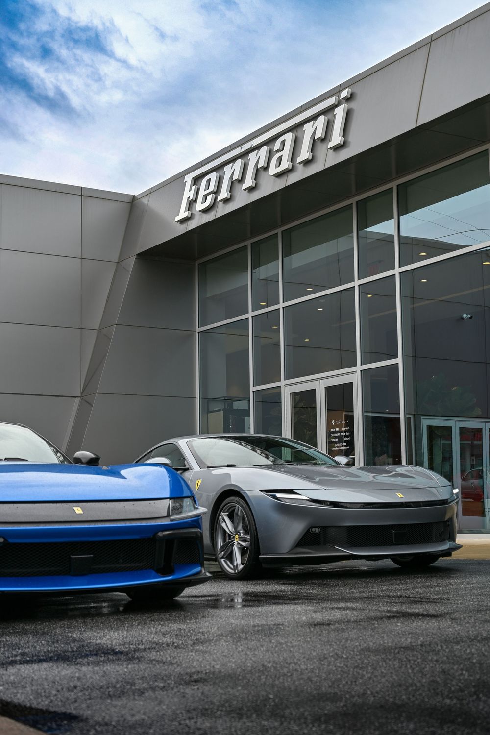 Low-angle view of modern luxury sports cars parked outside a sleek Ferrari dealership building under blue skies.