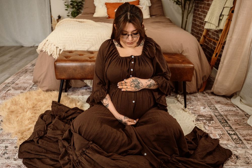 Person in brown dress poses on couch in cozy living room setting with decorative pillows and plants.