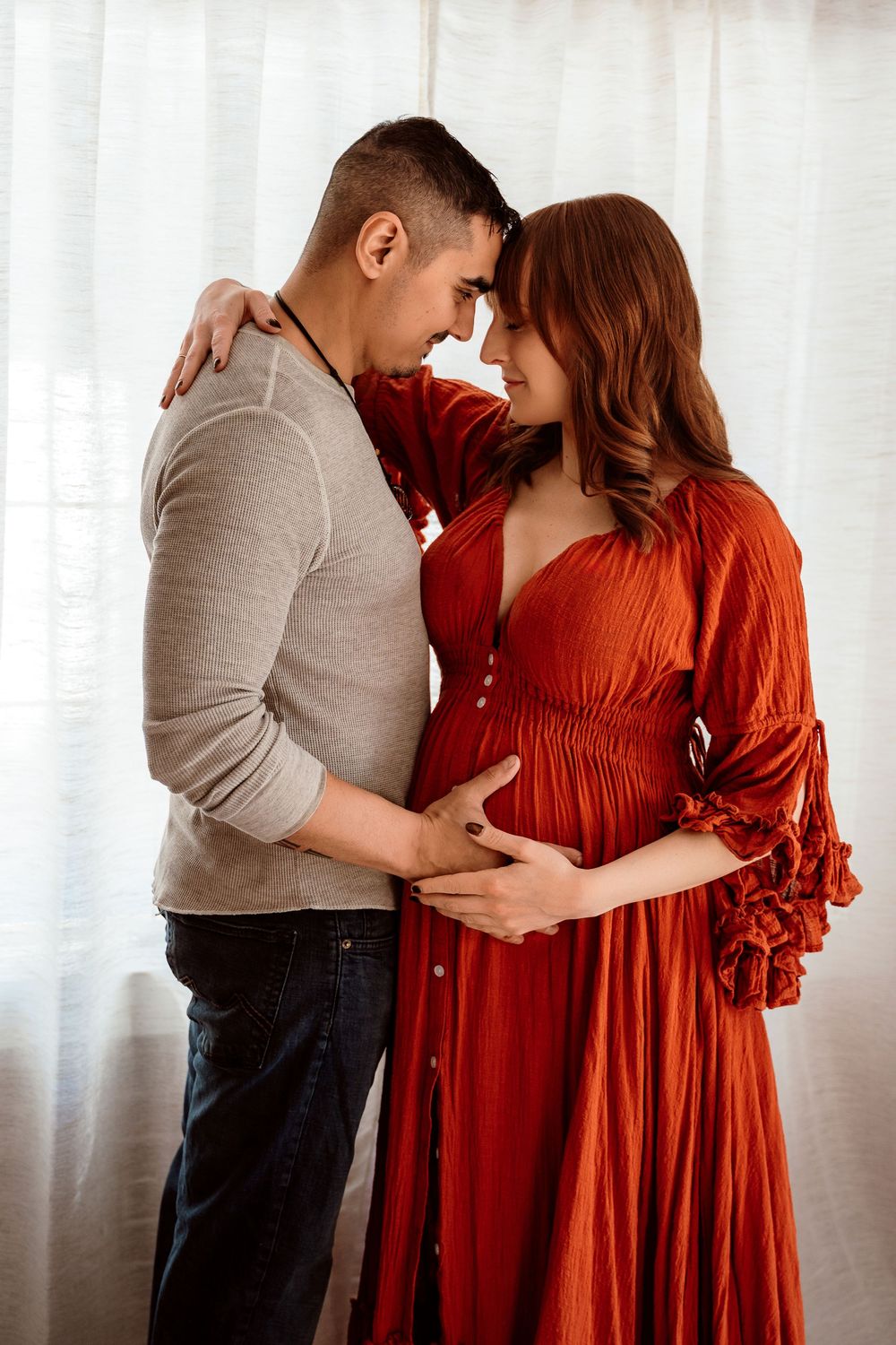 A couple sharing an intimate moment, the pregnant woman in a red dress with her partner tenderly holding her baby bump.