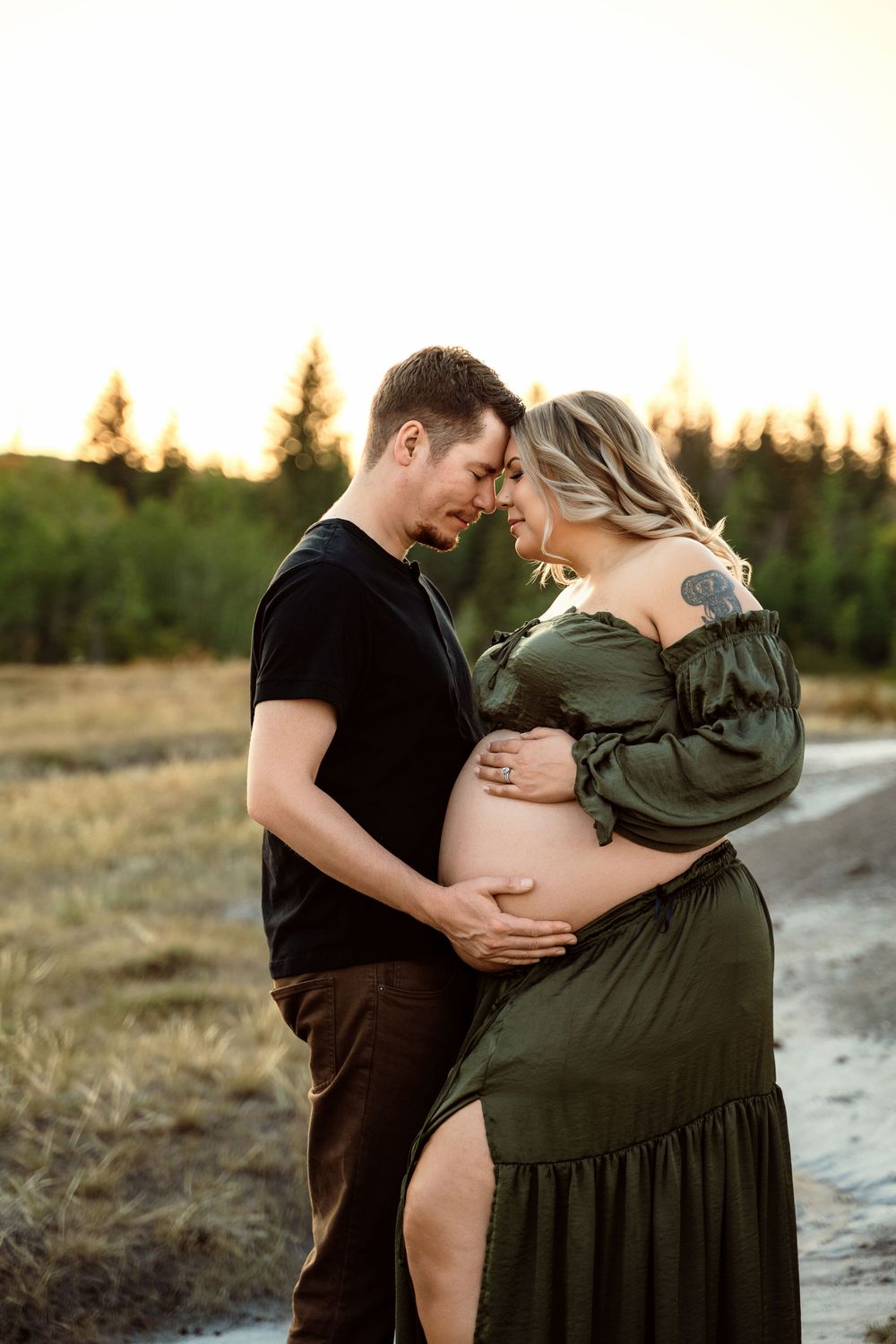 Couple shares intimate moments in an outdoor maternity photoshoot during golden hour in a rural setting.