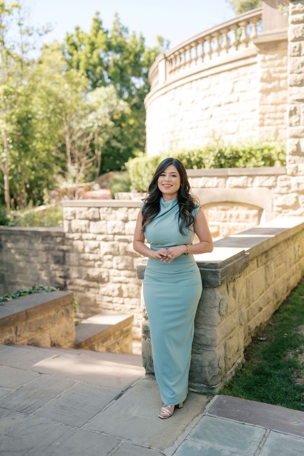 A series of romantic photos in front of a stone wall shows a couple in a mint green dress and navy suit.