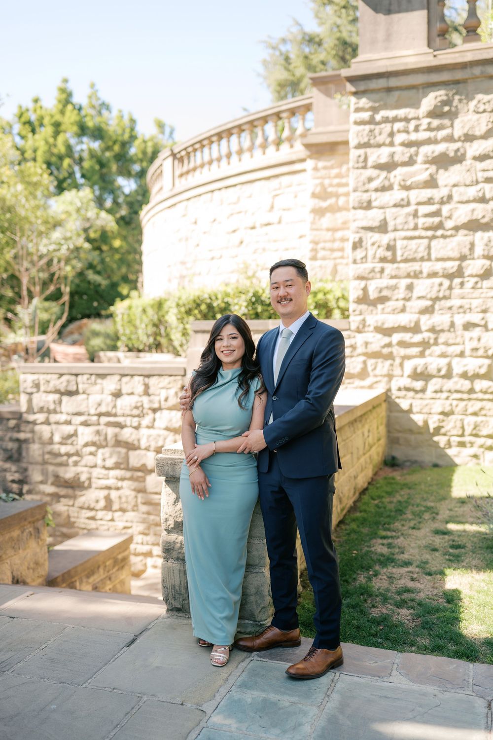A couple poses together against a stone wall backdrop in a series of romantic outdoor portraits.