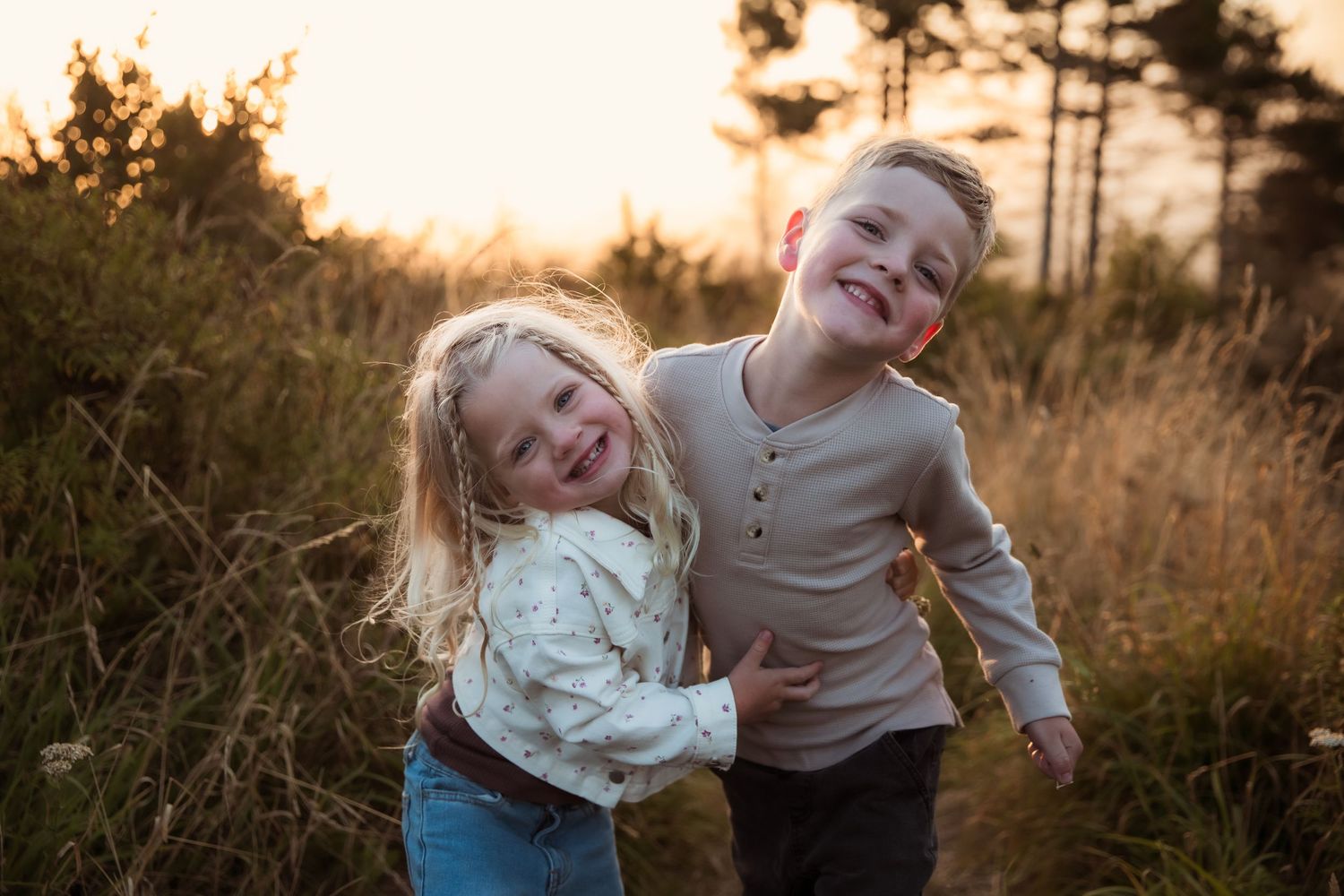 candid photo showing playful moments between siblings in a golden field at sunset.