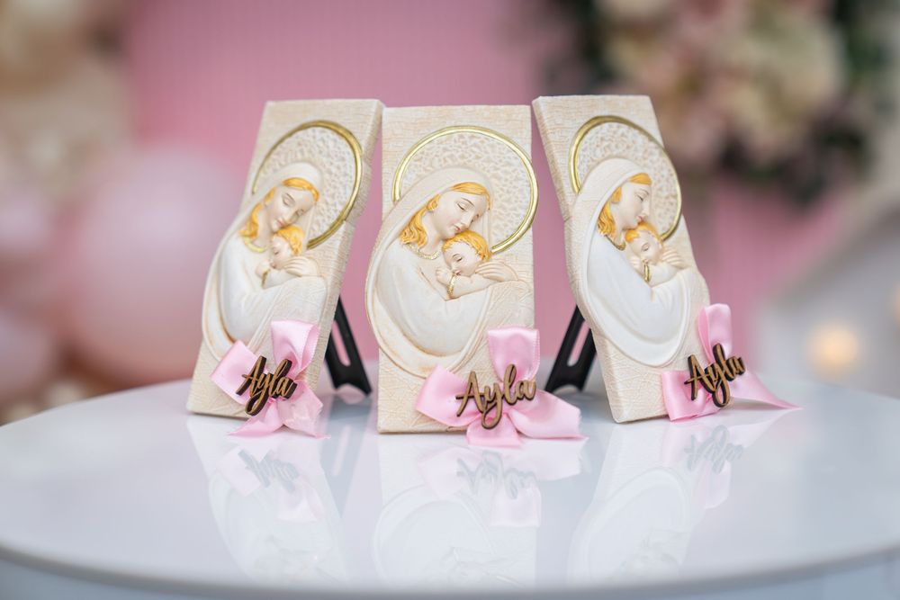 Three religious Madonna and Child keepsakes with pink bows and gold name tags displayed on a white surface.