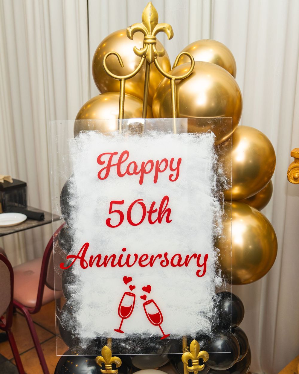 Gold balloon arch frames a Happy 50th Anniversary sign with champagne glasses, perfect for a golden anniversary celebration.