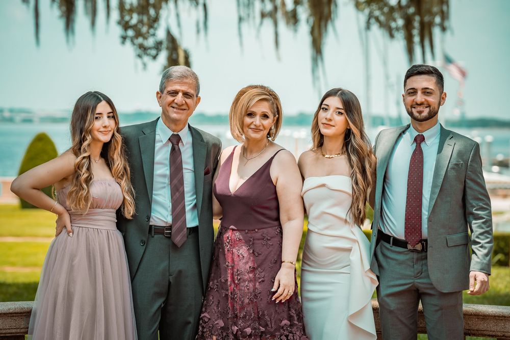 Family of five posing elegantly outdoors near waterfront, dressed in formal attire for a special occasion.