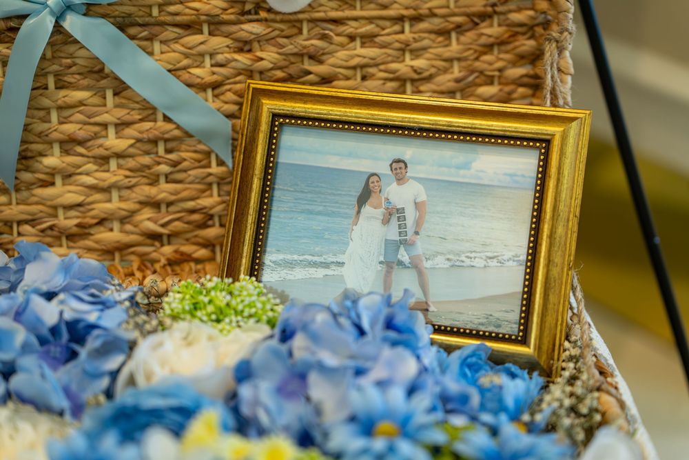 Gold framed photo of a couple on a beach surrounded by blue hydrangeas in a wicker basket.