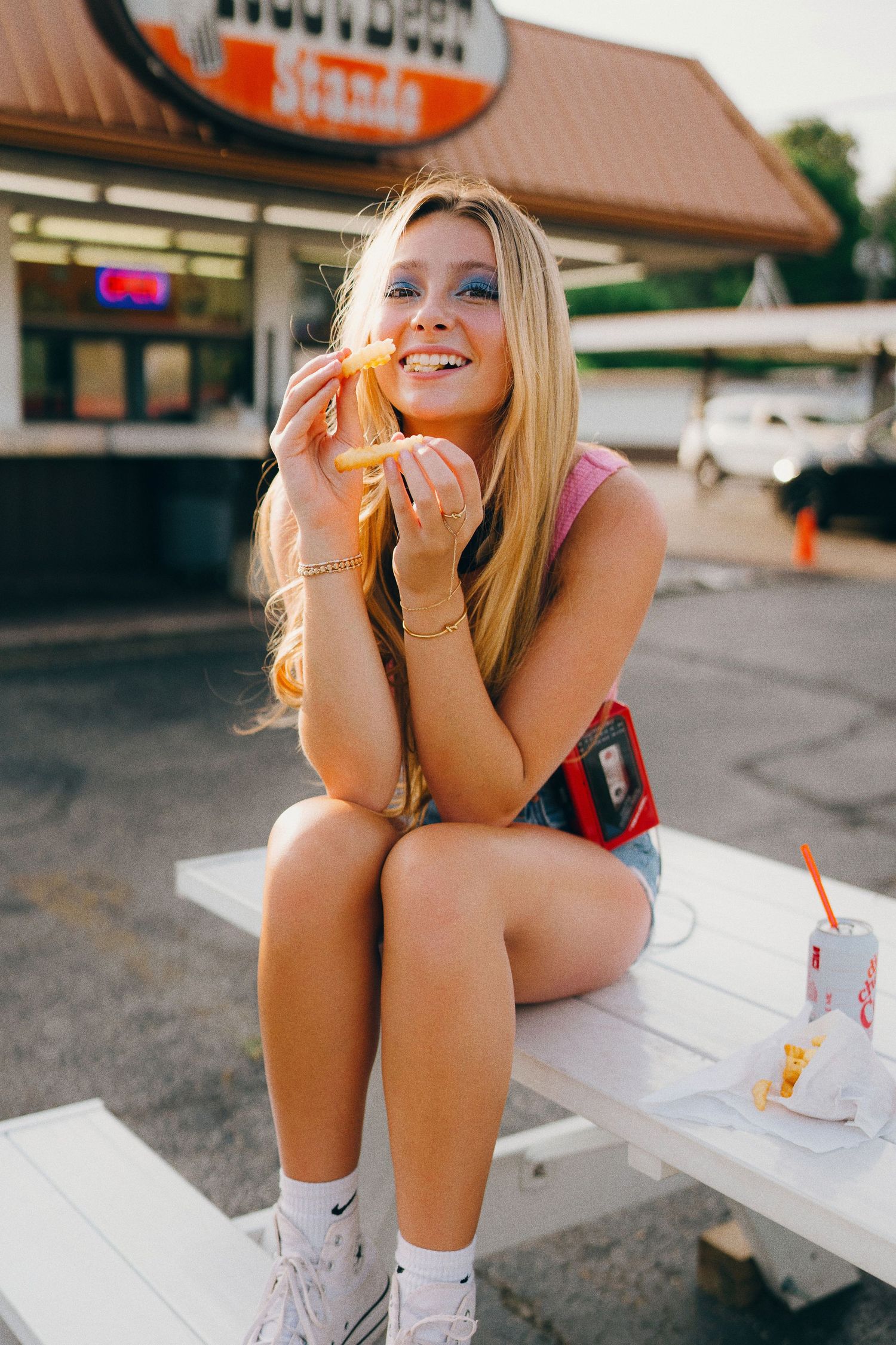 Person sitting outside a fast food restaurant at dusk enjoying a drink and french fries on a summer evening.