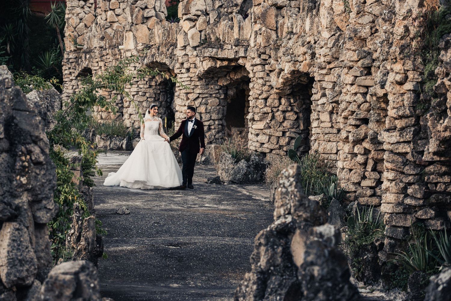 A stone archway walkway with rustic walls leads through a historic garden or castle grounds.