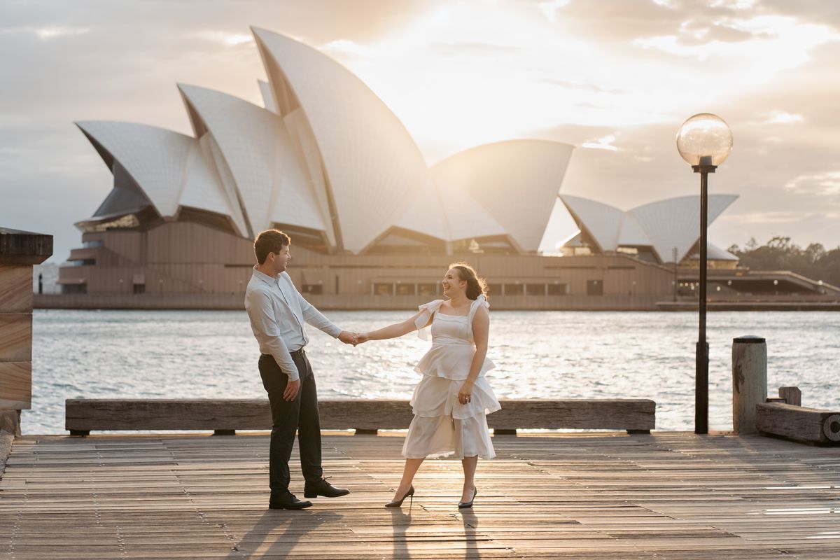 A couple dances together on a pier overlooking the iconic Sydney Opera House during sunset engagement photoshoot at the rocks
