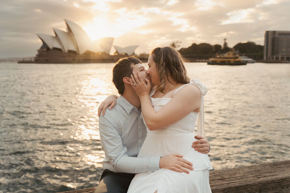A couple embraces during a romantic sunrise  photoshoot by the waterfront with cityscape views in the background at the Sydney The Rocks