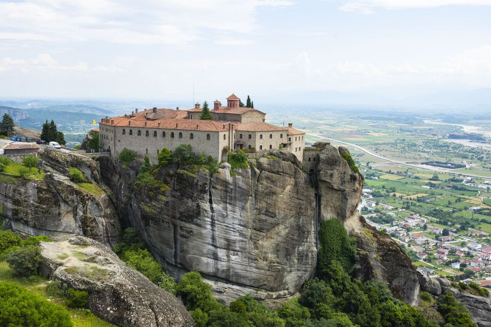 Ancient monastery perched atop dramatic cliffs at Meteora in Greece overlooking the valley and town below.