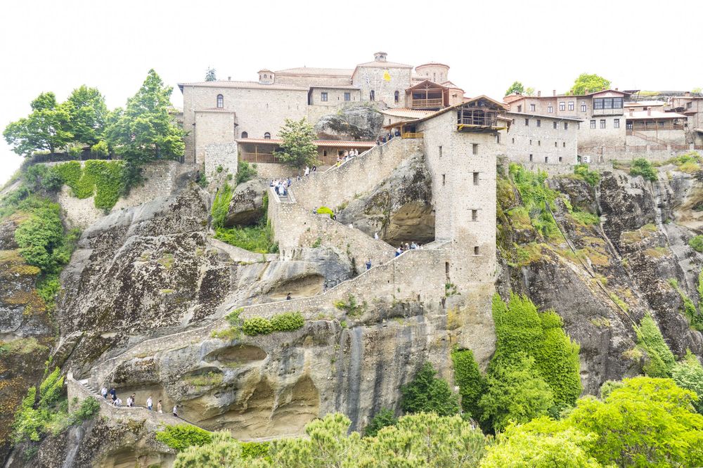 Ancient stone buildings and towers perched on steep rocky cliffs at the Meteora monasteries in Greece.