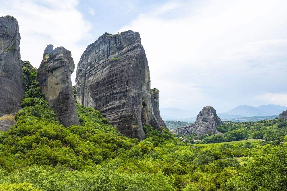 Towering sandstone rock formations rise above lush green forest at Meteora's famous monastic complex.