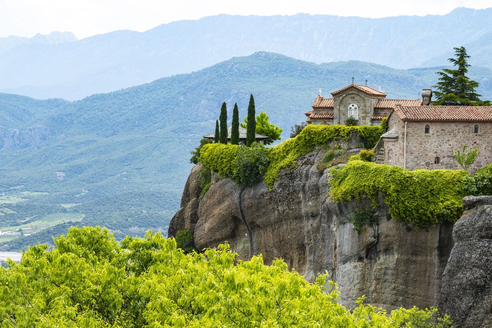 Ancient monasteries perched atop dramatic rocky cliffs in Meteora, Greece with mountains in the background.