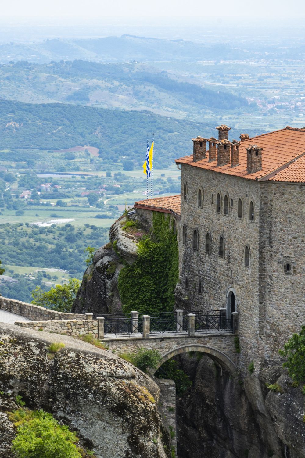 Medieval stone fortress perched on a rocky cliff overlooking a scenic mountain valley landscape with terracotta roofs.