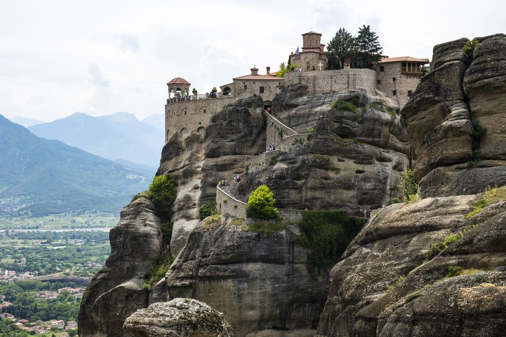 Ancient monasteries perched atop towering sandstone cliffs in Meteora, Greece against a backdrop of misty mountains.