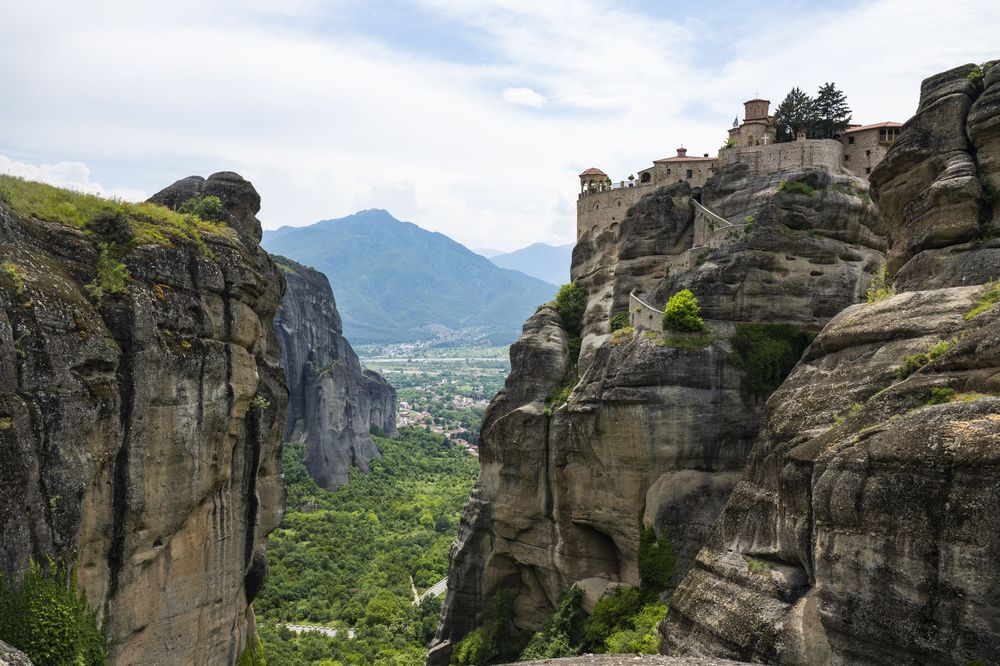 Dramatic rocky cliffs and monasteries of Meteora Greece rise above the valley with mountains in the background.