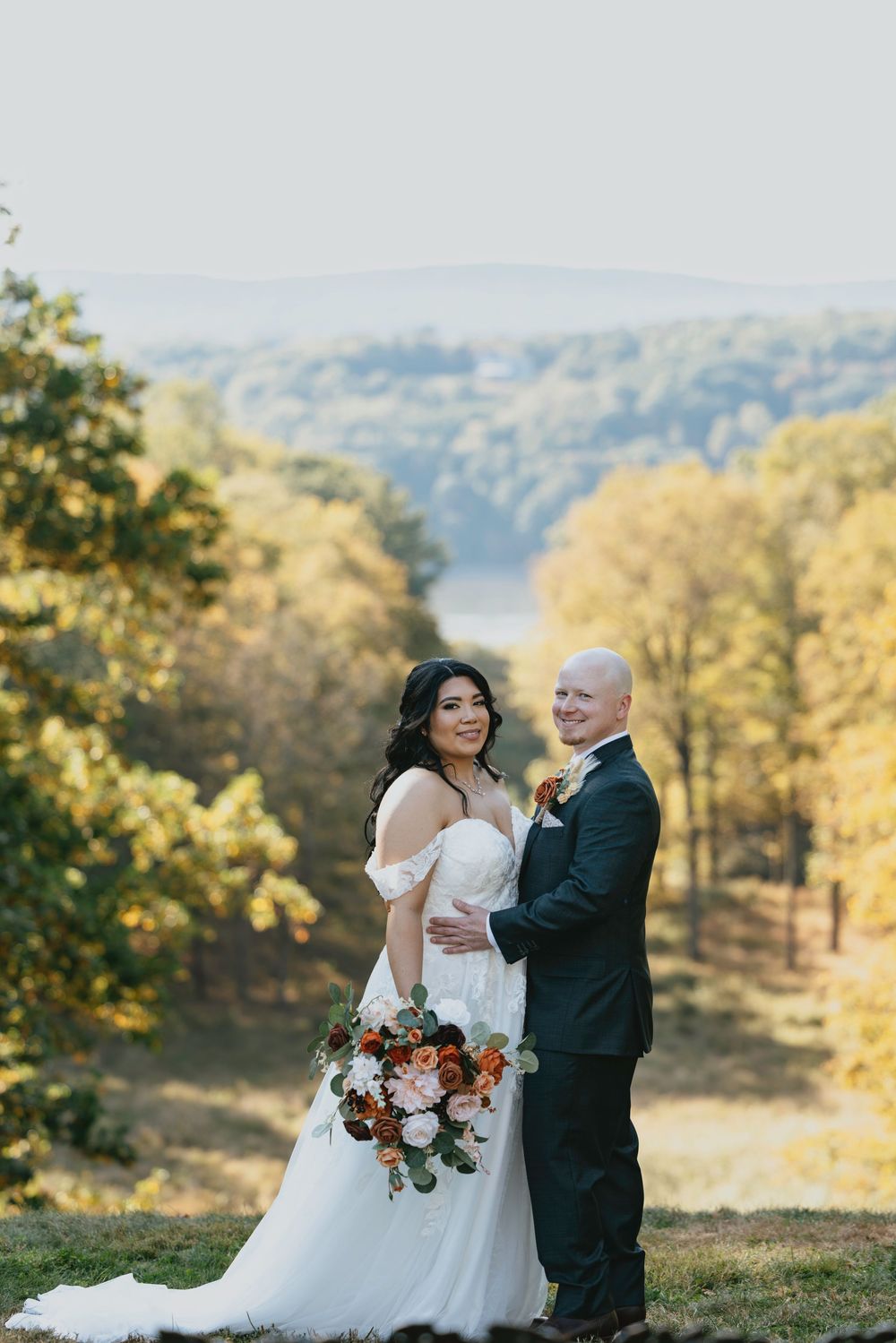 A couple shares a romantic moment in a scenic autumn setting with golden trees and rolling hills in the background.
