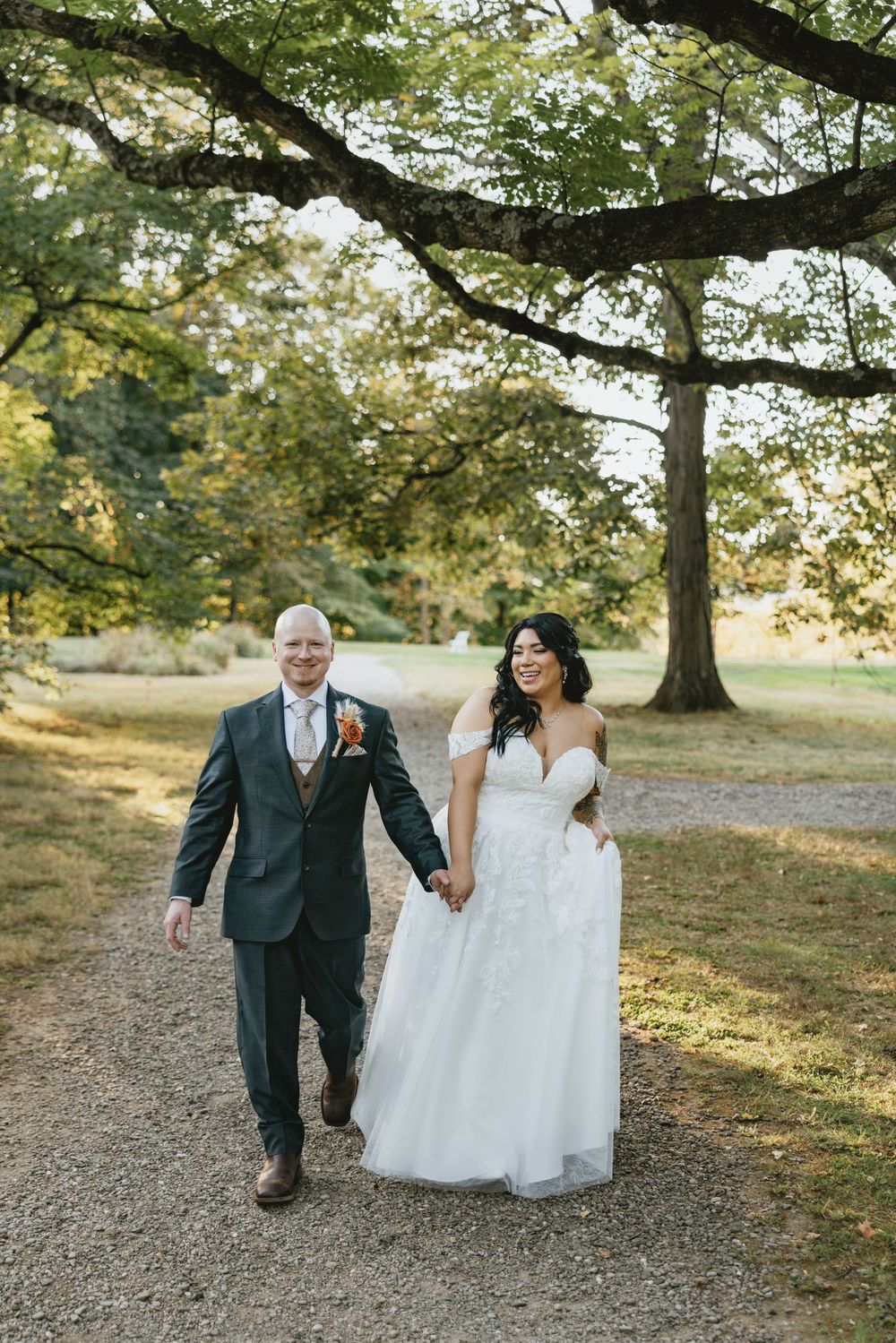A couple walks together on a tree-lined path during an autumn wedding photoshoot.