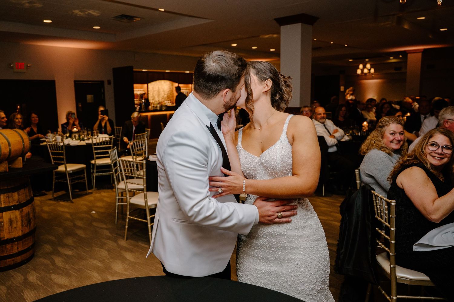 A group of wedding guests dance together on a dimly lit dance floor during an evening reception celebration.