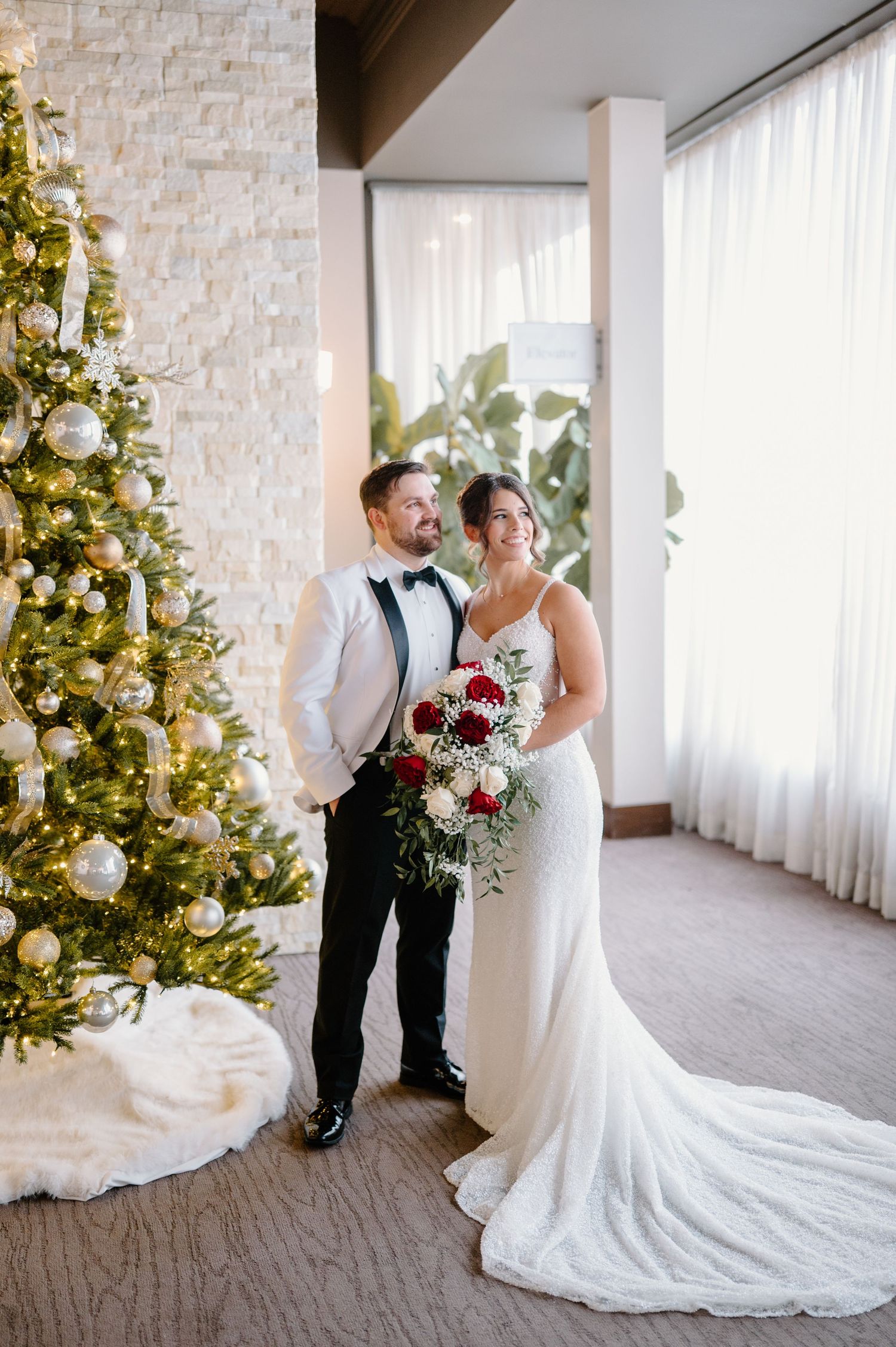 Elegant winter wedding scene with white decor, flowing curtains and decorated Christmas trees in the background.