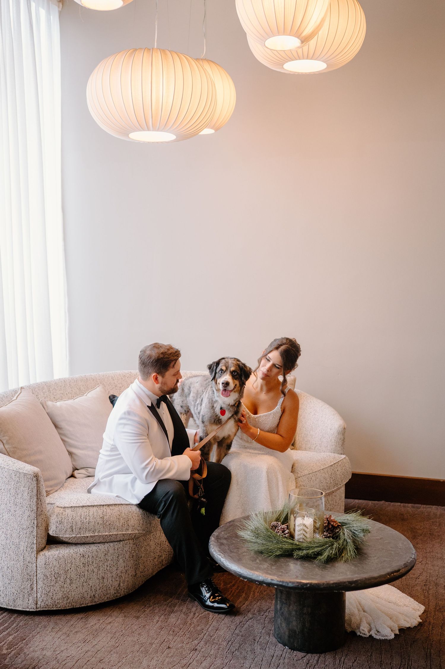 A couple in wedding attire shares a romantic moment on a curved sofa under glowing pendant lights.