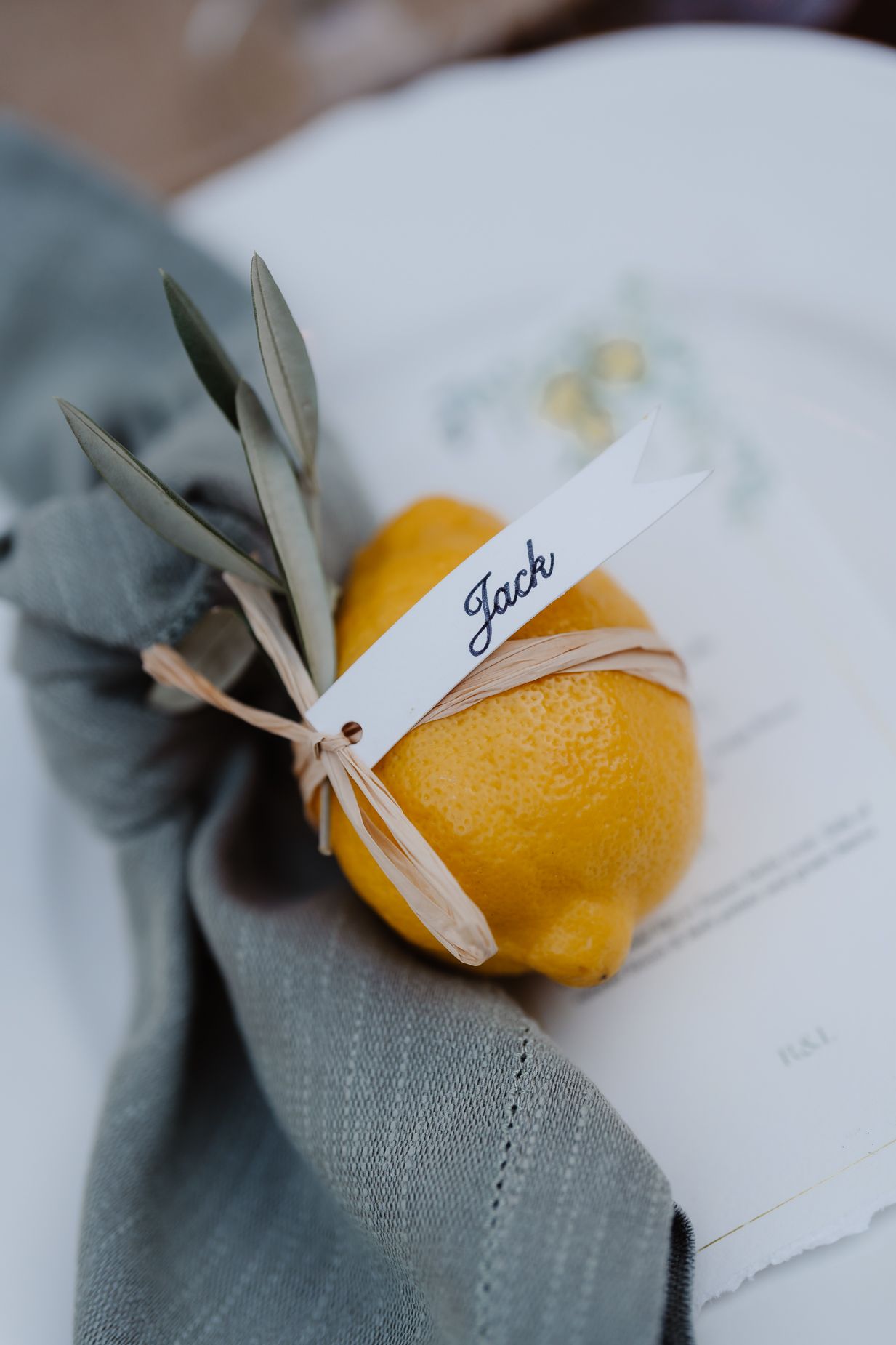 A fresh lemon with olive branches and name tag serves as a place setting decoration.