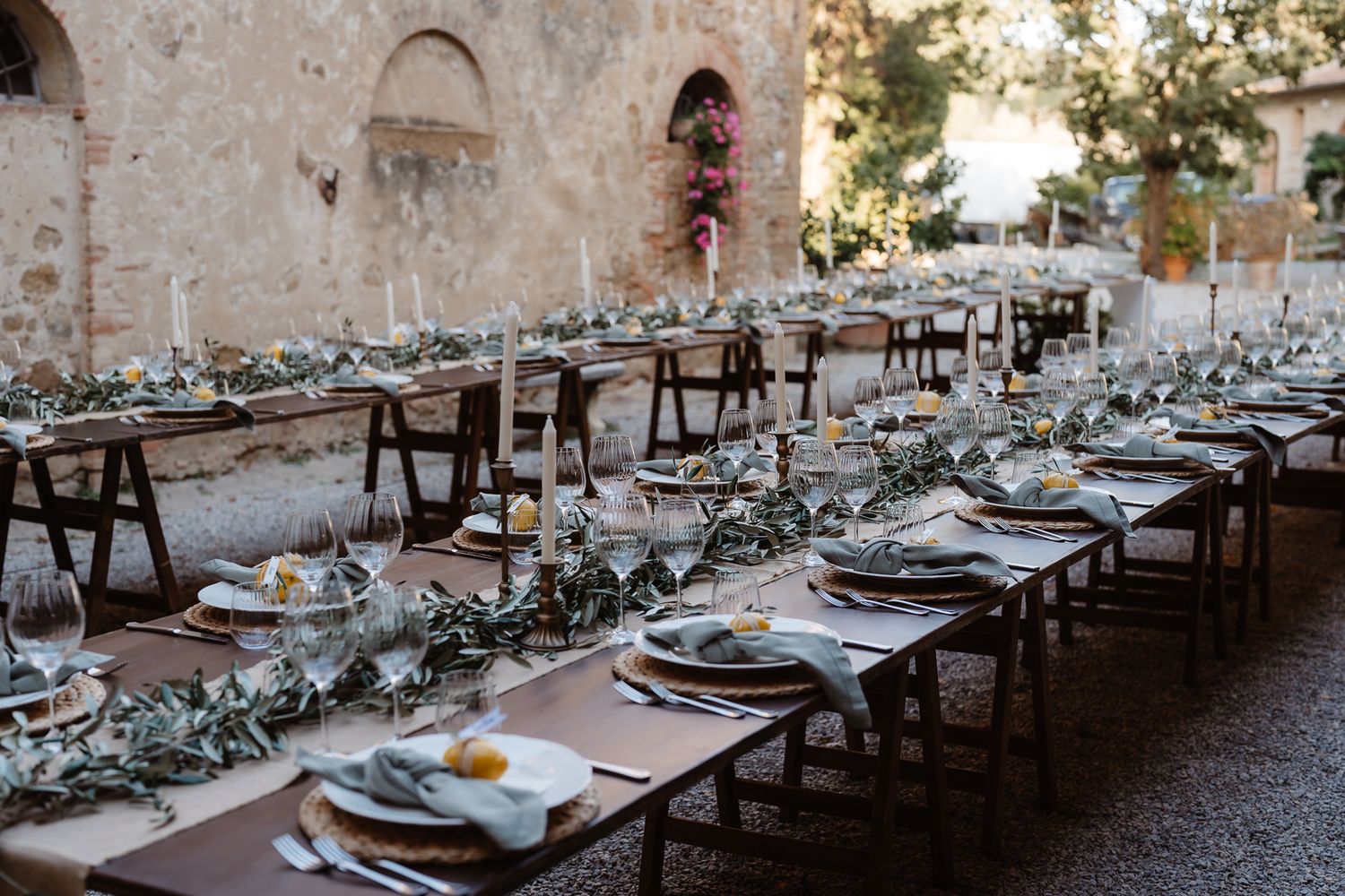 An elegant outdoor wedding reception setup with long tables and rustic stone wall backdrop.