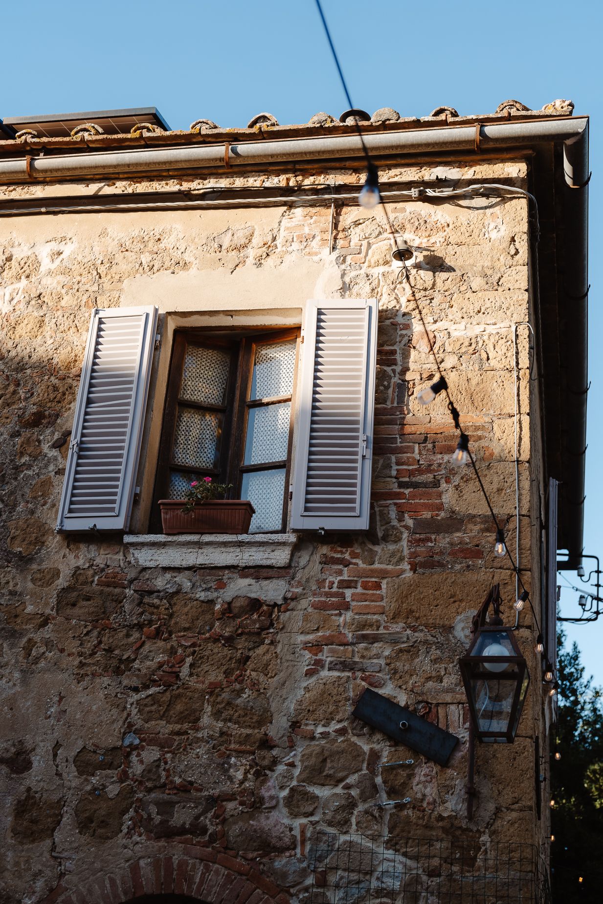 A rustic Italian window with gray shutters on weathered stone wall architecture.