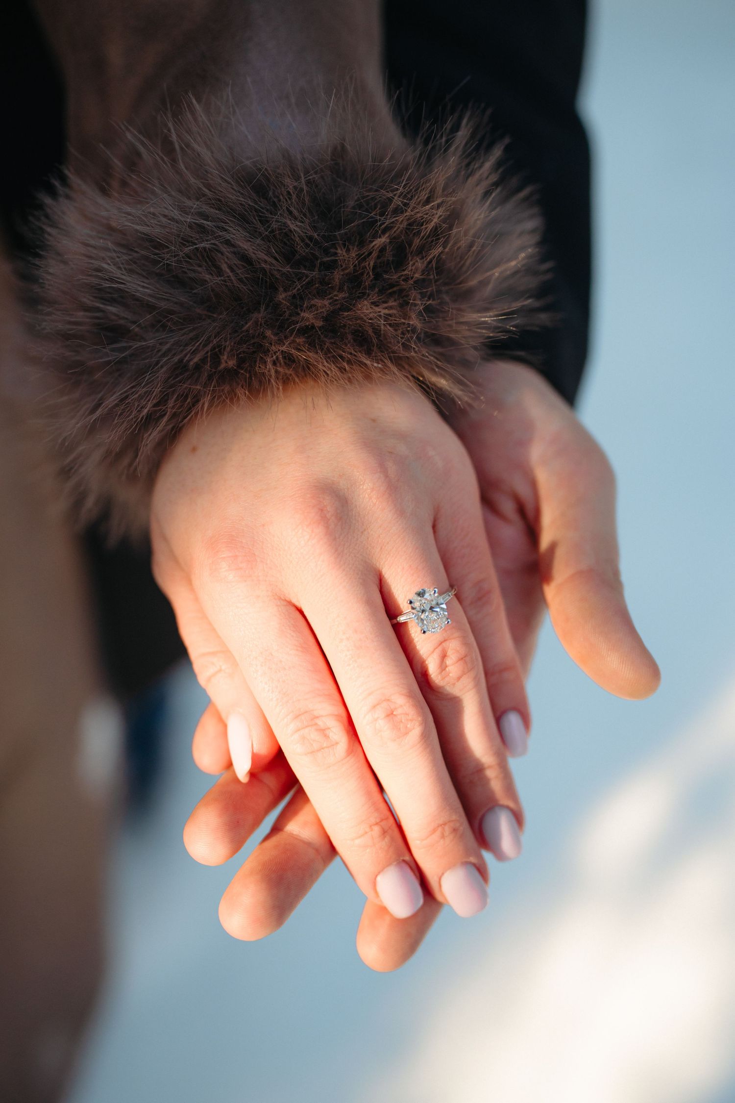 Close-up of hands with manicured nails showing off an engagement ring with a sparkling diamond solitaire.