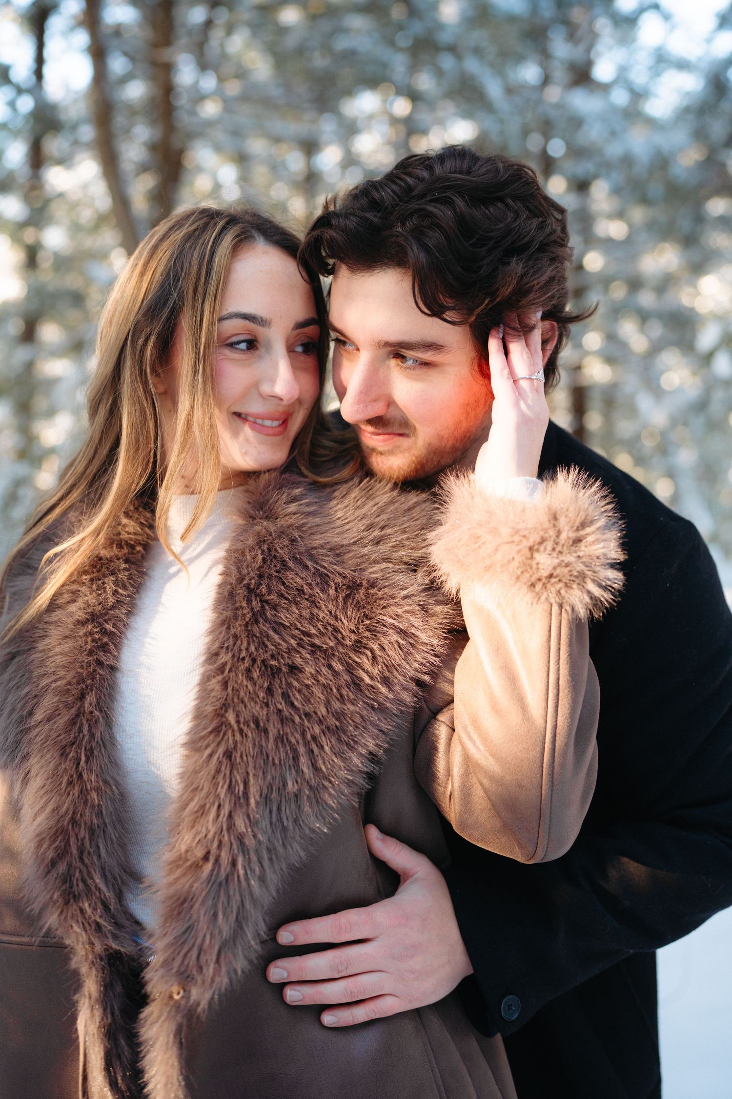 A romantic couple shares an intimate moment in a snowy forest wearing winter coats.
