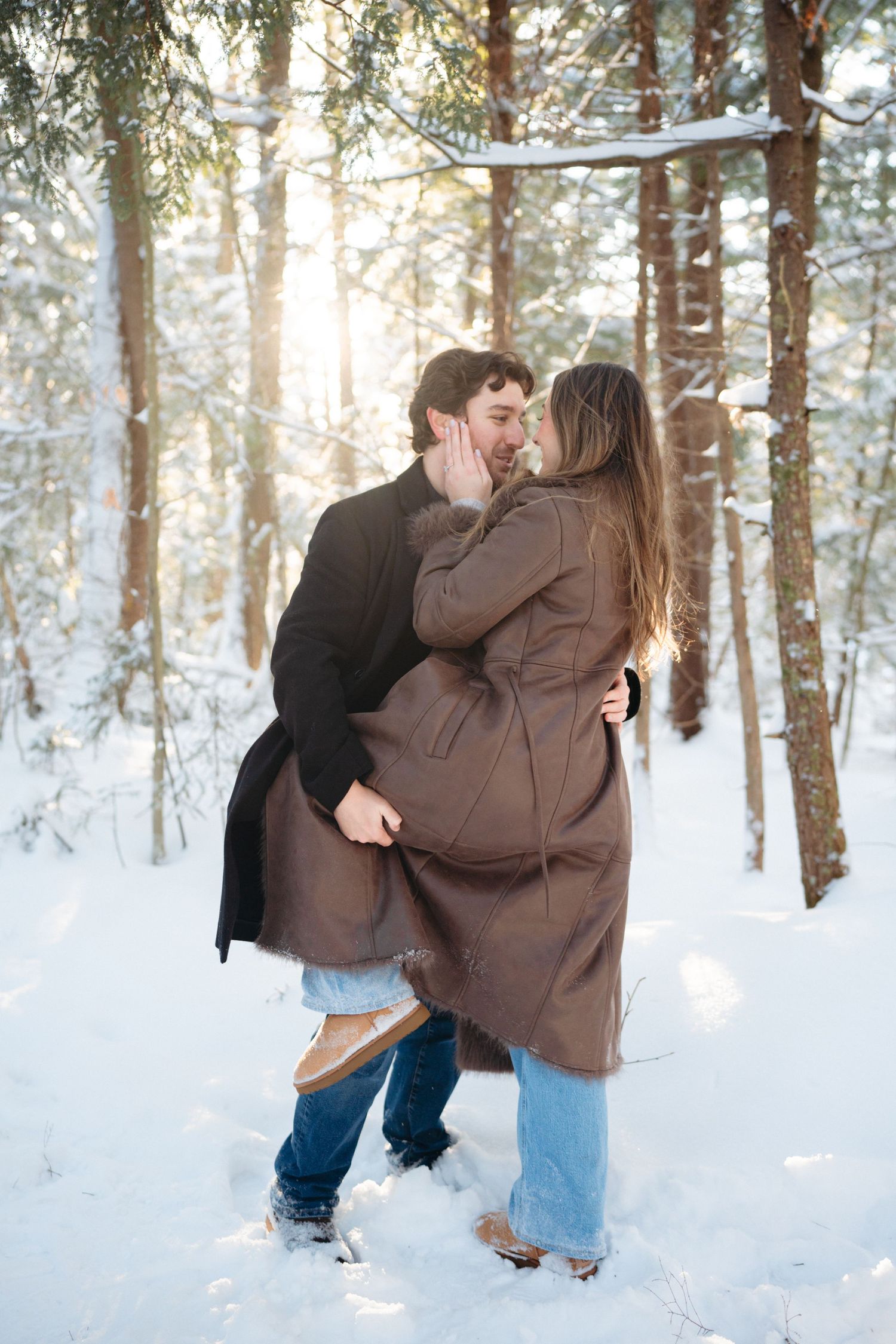A couple plays and laughs together in a sunlit winter forest with fresh snow on the ground.