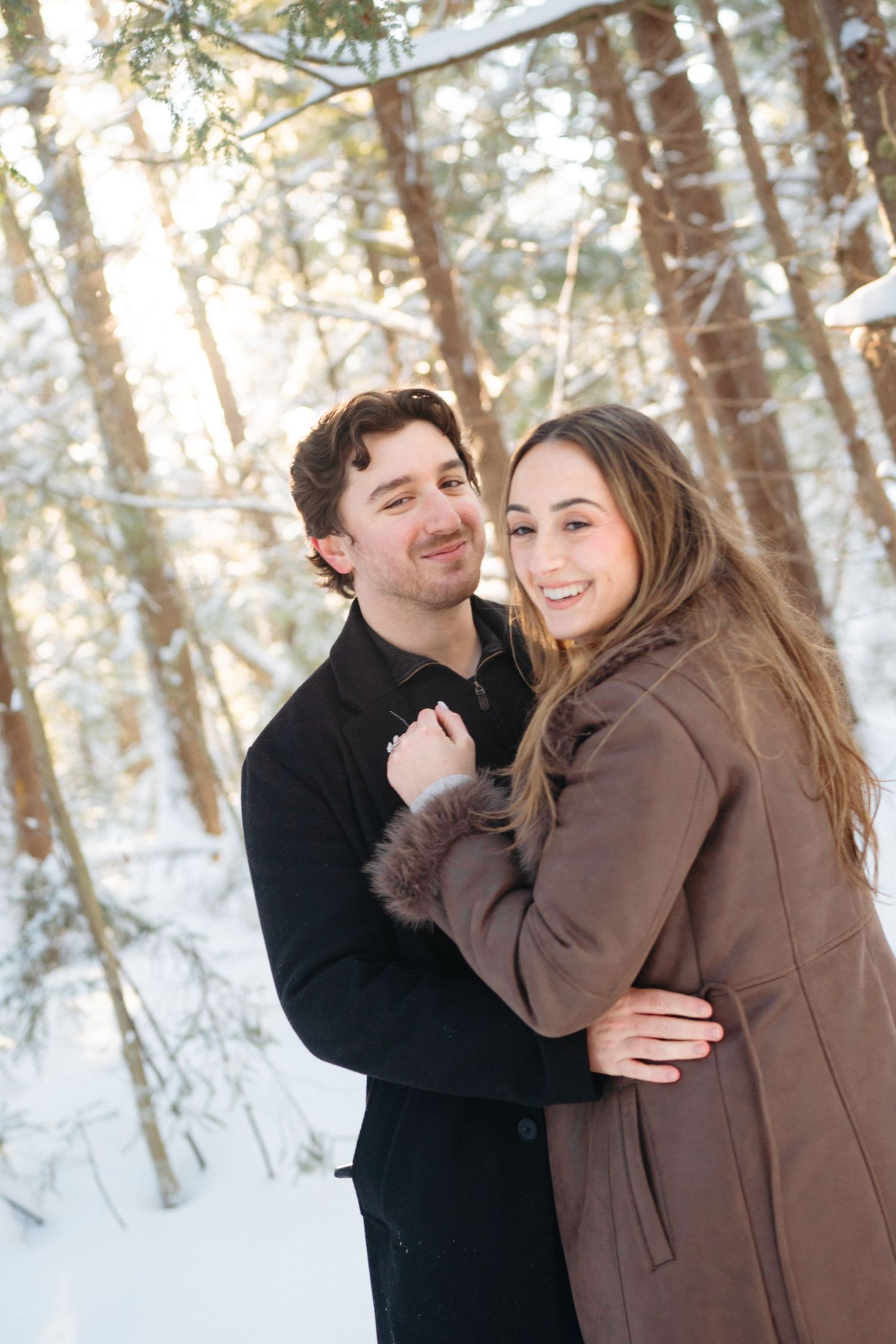 A loving couple shares joyful moments together in a snow-covered forest setting.